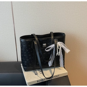 Macro detail of black tote bag with embossed pattern, pearl pendant and lace bow accessory