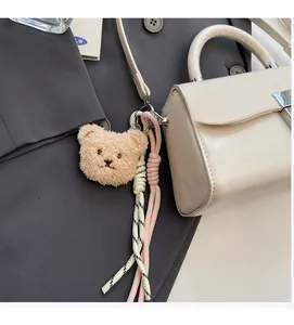 Cute beige plush bear keychain charm with colorful woven tassels on a handbag