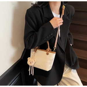 Detail of glossy beige bucket bag with brown leather trim and cute plush bear charm