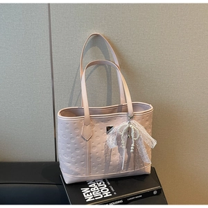 Close-up of pink embossed tote bag featuring lace bow and pearl pendant on a book