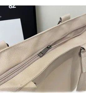 Detailed close-up of smooth metal zipper closure on a large beige canvas tote bag