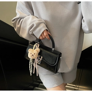 Detail of a vintage black leather handbag with silver rotary lock and a plush bear charm