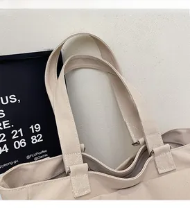 Detail of reinforced cross-stitched handles and metal ring on beige canvas tote bag