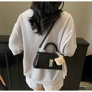 Detail of a black patent leather handbag with a silver square buckle and cute bear charm