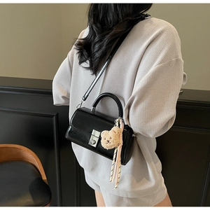 Detail of a structured black glossy leather handbag featuring silver twist lock and bear charm