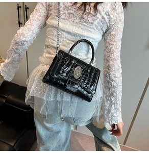 Detail of black crocodile texture bag with silver twist lock and metal chain strap