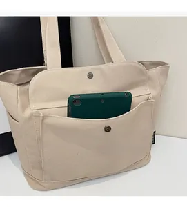 Close-up of beige canvas tote bag showing large front pocket and metal button detail