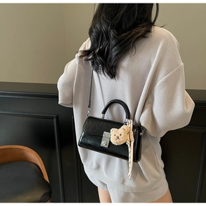 Glossy black faux leather handbag with cute plush bear pendant shown on model