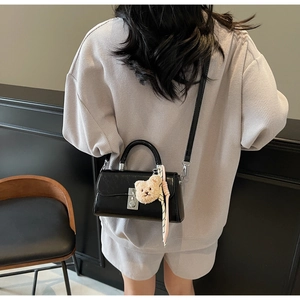 Detail showing a black crossbody bag with silver twist lock and cute teddy bear charm accessory