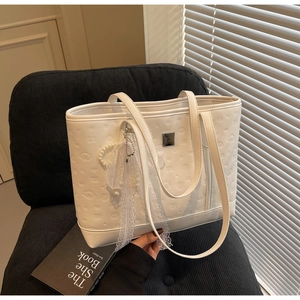 Detail of white embossed tote bag with lace bow and pearl charm on a black chair