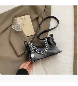 Detail of black glossy shoulder bag with chunky silver chain and brand logo on a coat