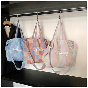 Three colorful checkered tote bags with Mearey embroidery hanging on a metal rack