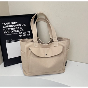 Detail view of large beige canvas tote bag with front flap pocket and side compartments