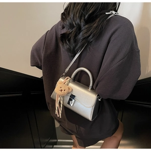 Silver mini square handbag with plush bear charm worn by model in a stylish city setting