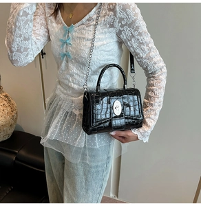 Detail of black crocodile embossed bag with silver metal clasp and chain strap