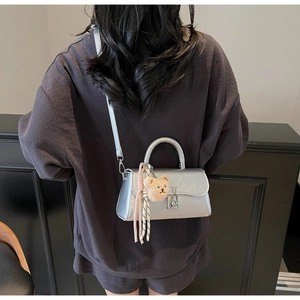 Detailed view of silver metallic handbag with plush bear charm worn by a model