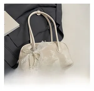 Detail view of a beige faux leather underarm bag with a lace pearl bow charm