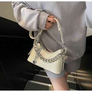 Detail of glossy beige patent leather underarm bag with thick silver chain on an escalator