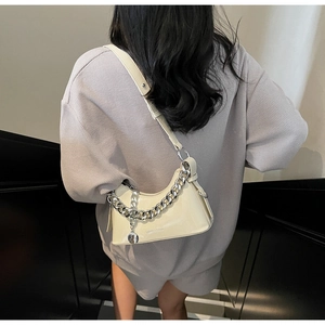 Detail of a creamy glossy crescent bag with chunky silver chain shown on model