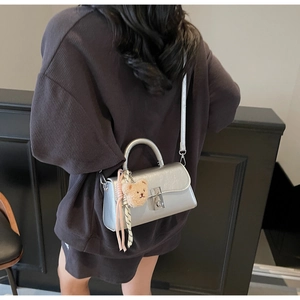 Silver metallic shoulder bag with plush bear charm and ribbon on model in grey outfit