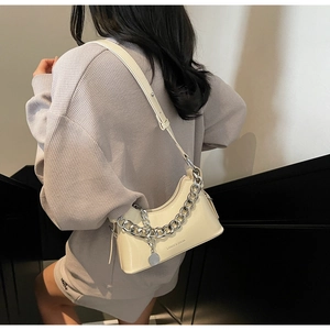 Detail view of cream glossy crescent bag with chunky silver chain and adjustable strap