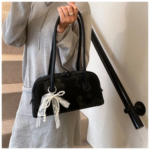 Glossy black underarm bag featuring white lace and pearl bow charms on a staircase