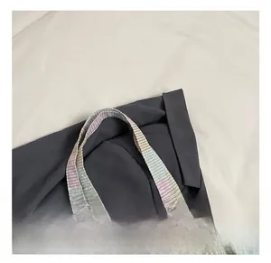 Close-up of multicolor striped woven handles on a canvas tote bag with a gray blazer