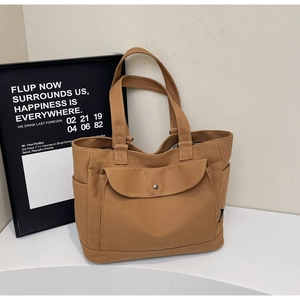 Close-up of brown canvas tote bag featuring front snap-button pocket and side compartment