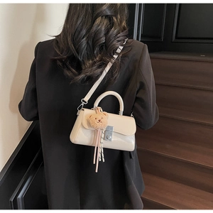 Detail of a beige PU leather mini bag with a plush bear charm and long fringe tassels