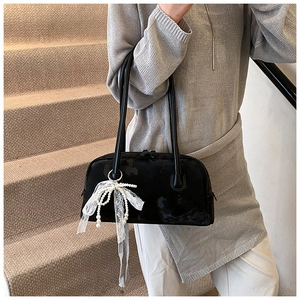 Detail of elegant black glossy underarm bag with white lace bow and pearl pendant charm