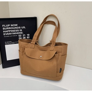 Detail of tan canvas tote bag showing the front pocket with metal snap and durable texture
