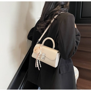Detail of minimalist beige faux leather square bag with metal clasp and plush bear charm