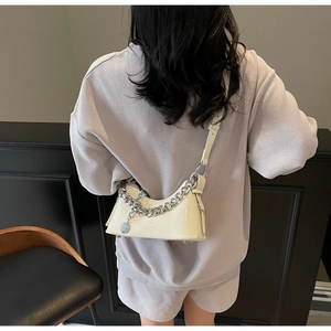Close-up of glossy cream patent leather bag with silver chain and brand engraving