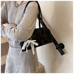 Detail of glossy black shoulder bag with pearl lace bow charm on a person at stairs