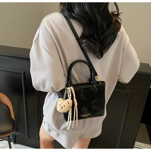 Detail of black glossy crossbody bucket bag with plush bear charm on a female model