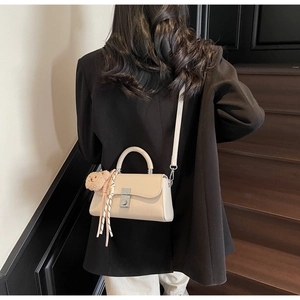 Model wearing a chic beige crossbody mini bag with a plush bear charm and striped ribbon detail