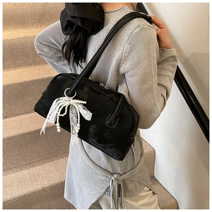 Detail of a black Boston bag with a white lace and pearl bow charm on leather surface