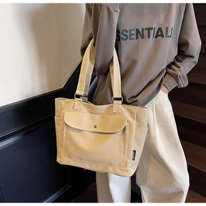 Detailed view of beige canvas tote bag showing metal snap pocket and sturdy fabric texture