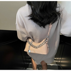 Glossy pale pink underarm bag with silver chain strap shown on a model on stairs