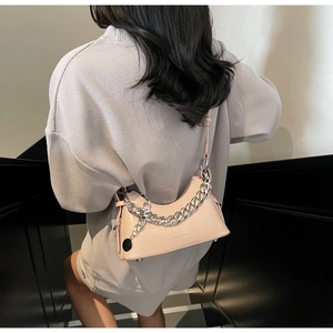 Detail of pink glossy crescent bag with silver chain worn over the shoulder by a model