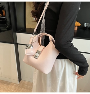 Detailed shot of a light pink glossy bucket bag with silver heart charm on model