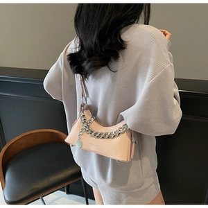 Detail view of a pink glossy underarm bag with a bold silver chain on a model