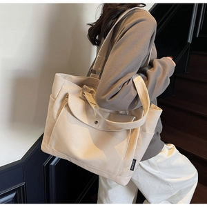 Detailed view of cream canvas tote bag with front flap pocket and side storage compartment