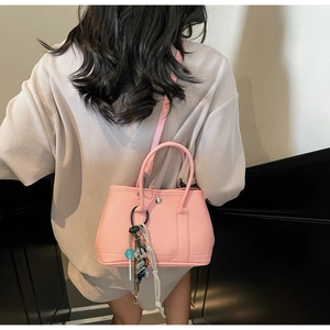 Detail der rosa Bucket Bag aus Litschi-Leder mit Bärenanhänger und gewebter Kette