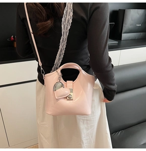 Detail of light pink bucket bag featuring lace shoulder strap and heart pendant accessory