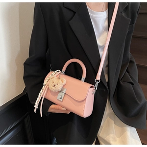 Pink leather handbag with striped scarf and teddy bear charm on dark wooden stairs
