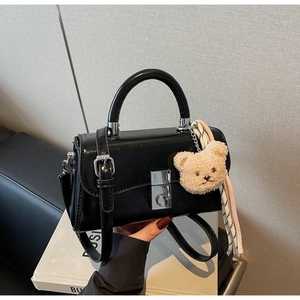 Detail of black patent leather bucket bag featuring a plush bear charm and silver clasp