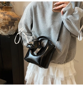 Detail of black glossy bucket bag featuring silver square buckle and heart charm on a model