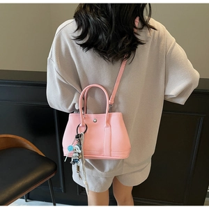 Rosafarbene Eimertasche mit Litschi-Maserung und Bärenanhänger im modernen Straßenstil