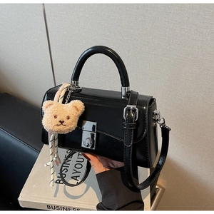 Detail of black glossy leather handbag with silver rotary lock and bear charm accessory